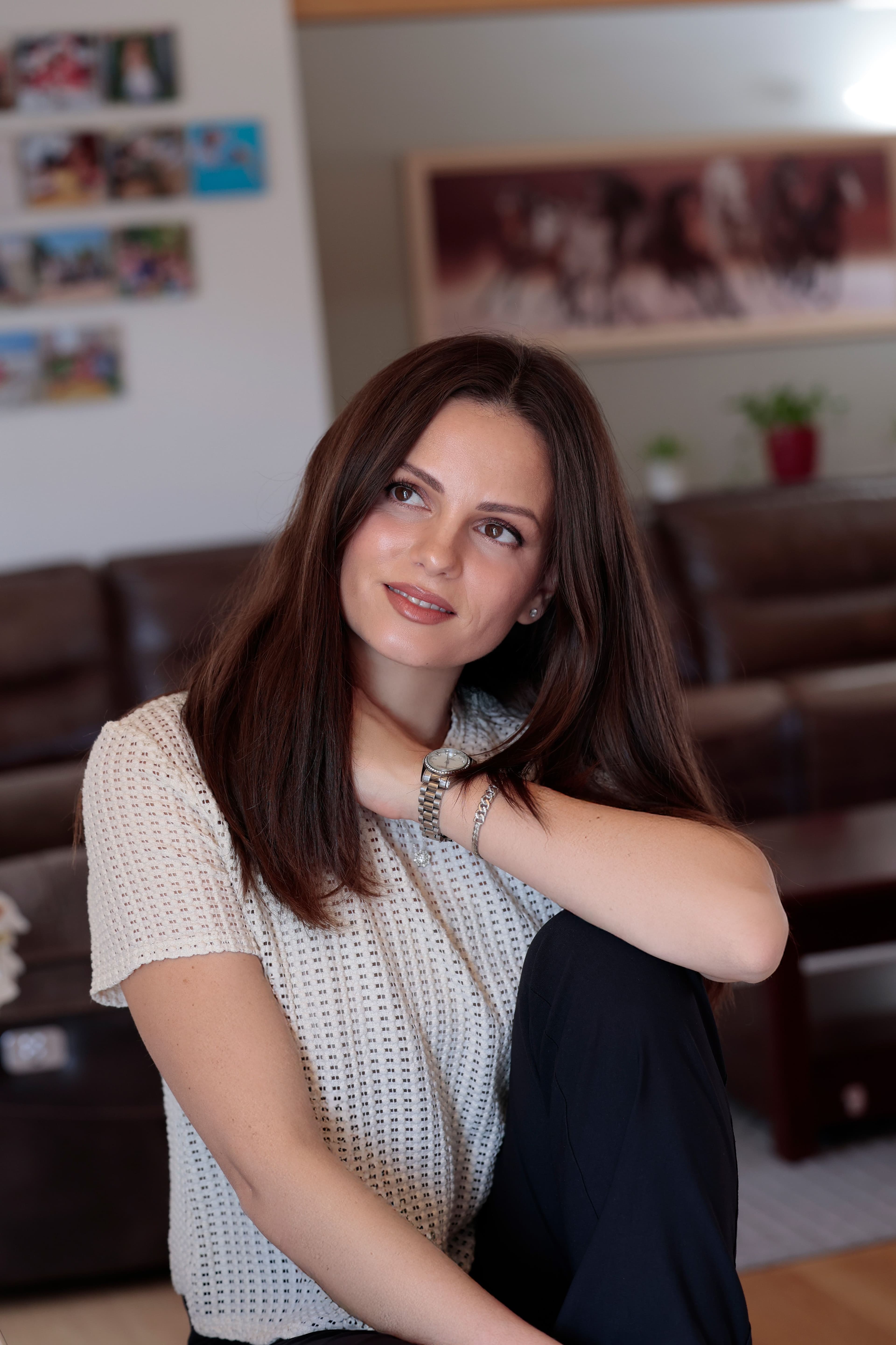 Portrait of a woman with long brown hair resting her hand at her neck and looking off to the side.