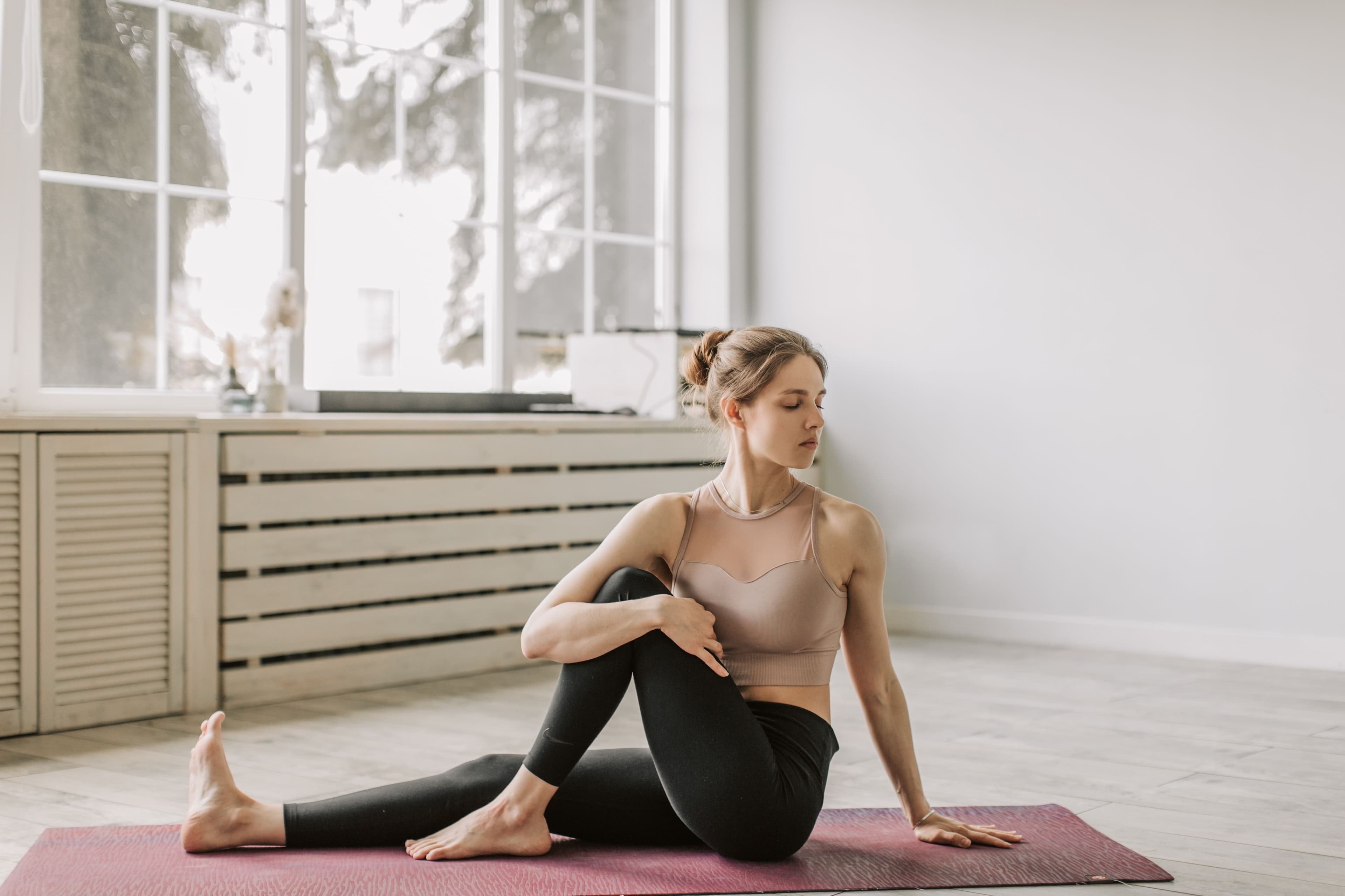 A woman seated on a mat in a bright, airy room, turning gently in a seated twist.